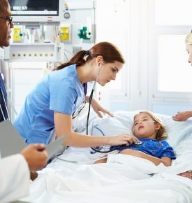 Enfermera atendiendo a una niña en una cama de hospital, utilizando un estetoscopio mientras otros profesionales observan.